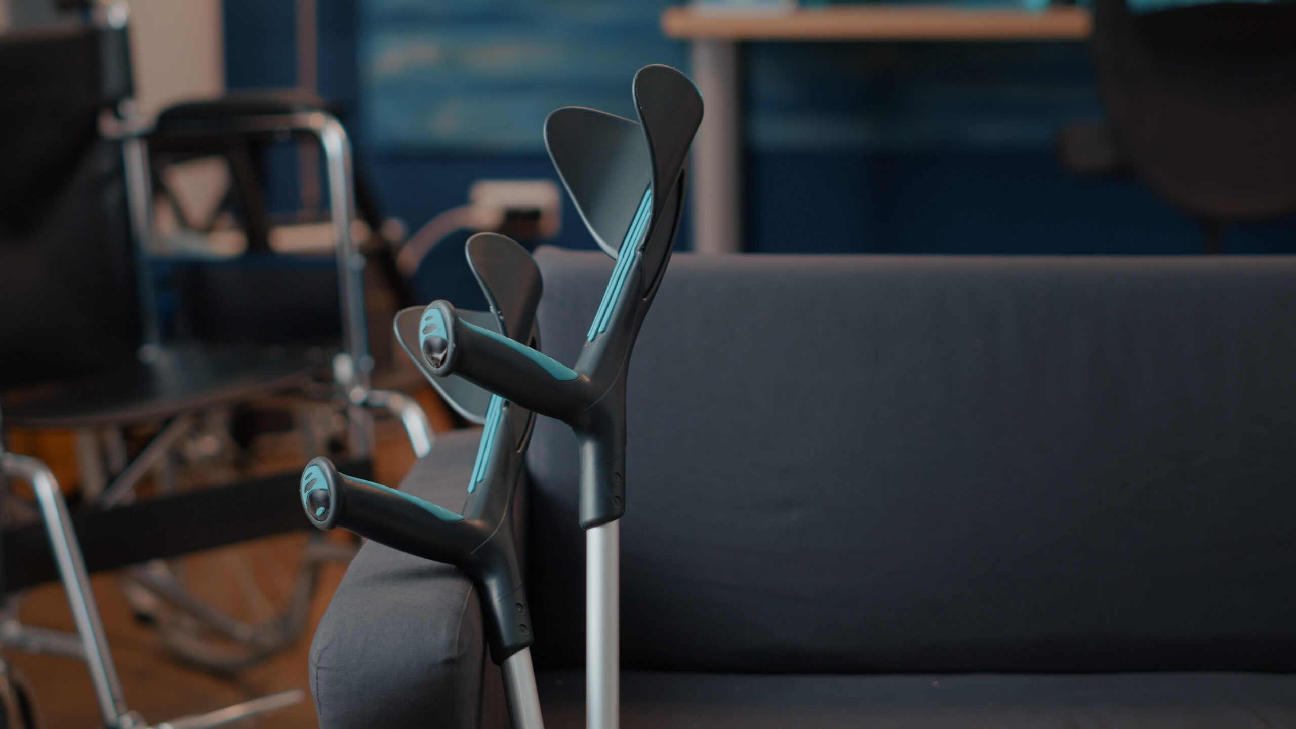 Trzy kijki narciarskie ustawione obok siebie na szarej kanapie w pomieszczeniu.