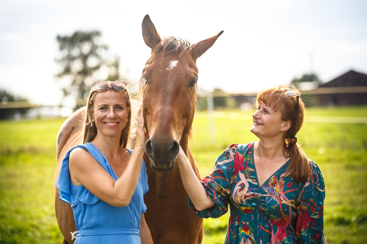 Dwie kobiety i koń na zielonym pastwisku, kobiety głaszczą konia, uśmiechają się i cieszą się wspólnym czasem na św