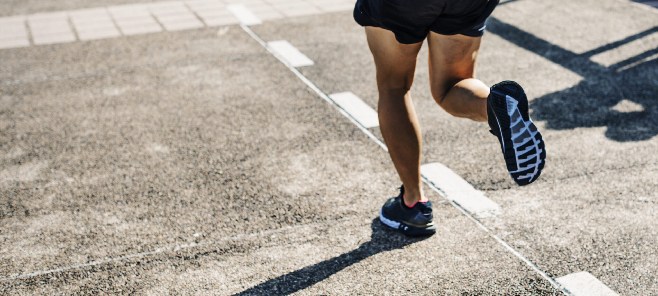 Biegacz w czarnych butach i szortach startuje na torze lekkoatletycznym w słoneczny dzień.