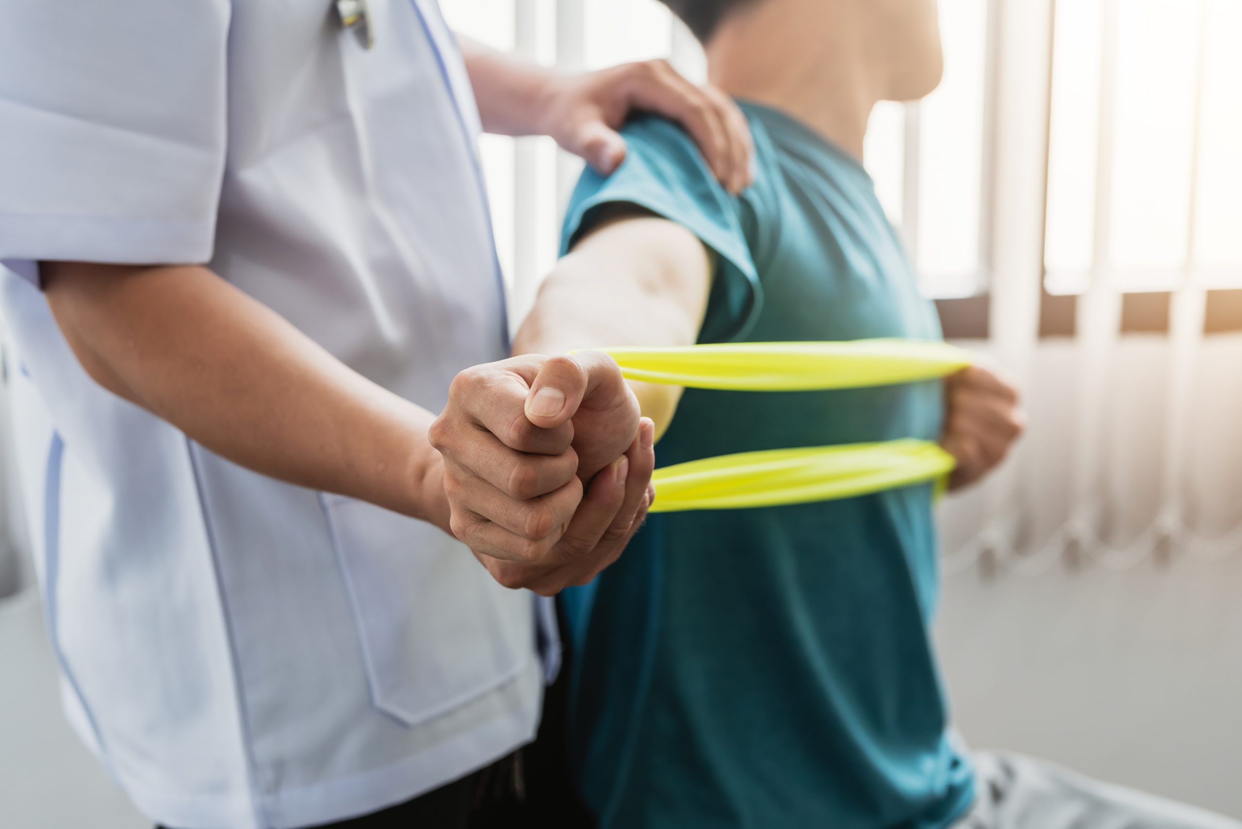 Terapeuta pomaga pacjentowi w ćwiczeniach, trzymając jego rękę i wspierając go podczas rehabilitacji.