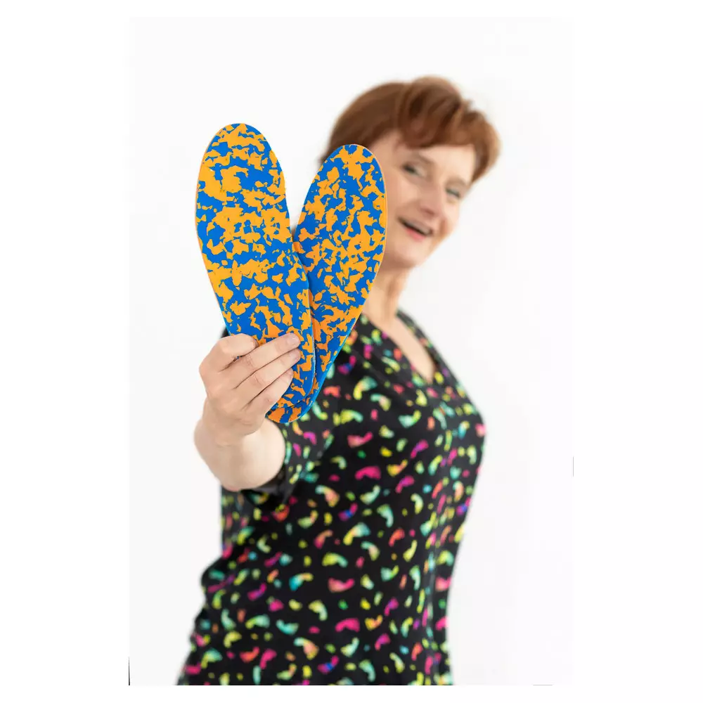 Kobieta trzyma w ręku buty do chodzenia z niebiesko-żółtym wzorem, uśmiecha się i patrzy w stronę kamery.