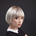 Młoda kobieta z krótką, blondynką fryzurą, patrząca na lewo, ubrana w czarną bluzkę z b whiteową kołnierzykiem.