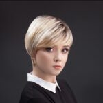 Młoda kobieta z krótkim blond włosem, ubrana w czarną bluzkę z b white kołnierzykiem, na ciemnym tle.