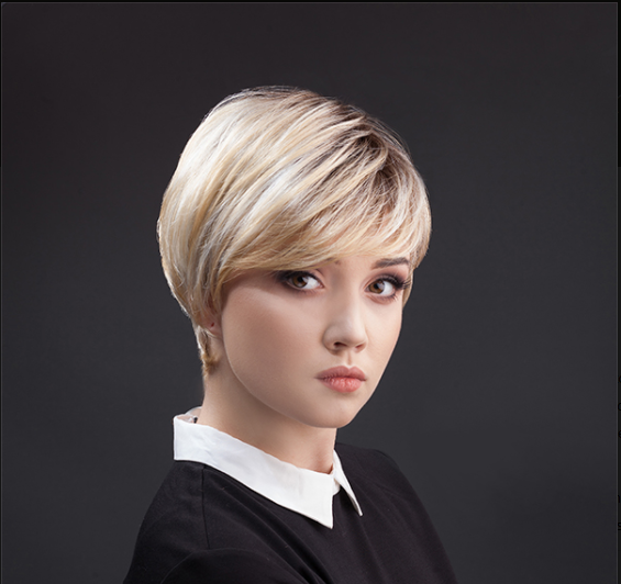 Młoda kobieta z krótkim blond włosem, ubrana w czarną bluzkę z b white kołnierzykiem, na ciemnym tle.