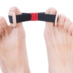 Stopy z palcami w górze, trzymające pasek od poduszki ortopedycznej z czarnym paskiem i białymi klamrami.