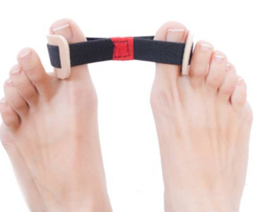 Stopy z palcami w górze, trzymające pasek od poduszki ortopedycznej z czarnym paskiem i białymi klamrami.