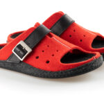 Czerwone kapcie z czarnym paskiem i metalową klamrą, wykonane z miękkiego materiału, na czarnej podeszwie.