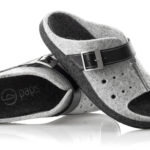 Szare kapcie z czarnymi wstawkami, regulowanym paskiem i miękkim wnętrzem, wykonane z filcu i skóry.