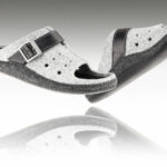 Kapcie z filcu i skóry z czarnymi paskami i metalową klamrą, uniesione nad odbiciem na białym tle.