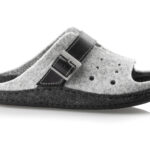 Szara kapcie z czarnym paskiem i metalową klamrą, wykonane z filcu, z otworami na palce, na czarnej podeszwie.