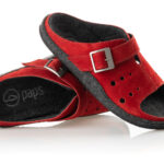 Czerwone kapcie z czarną wyściółką, regulowanym paskiem i perforacjami na górze.