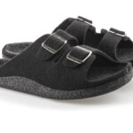 Czarne kapcie z dwoma regulowanymi paskami na metalowe klamry, wykonane z miękkiego materiału, na białym tle.