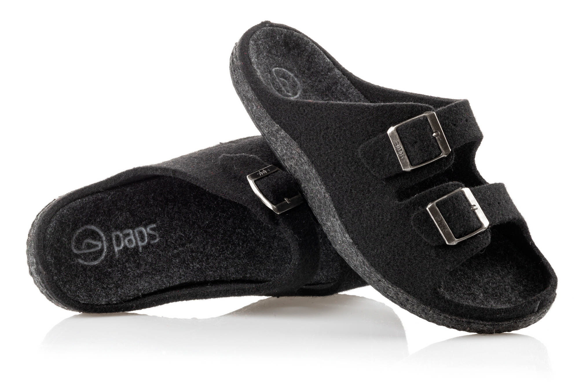 Czarne kapcie z dwoma paskami na rzepy i metalowymi klamrami, wykonane z miękkiego materiału, na białym tle.