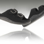 Czarne kapcie na rzepy z miękką podeszwą, uniesione nad odbiciem na białym tle.