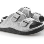 Szare kapcie z dwoma metalowymi klamrami i miękkim, filcowym materiałem, na czarnej podeszwie, ustawione na białym tle.