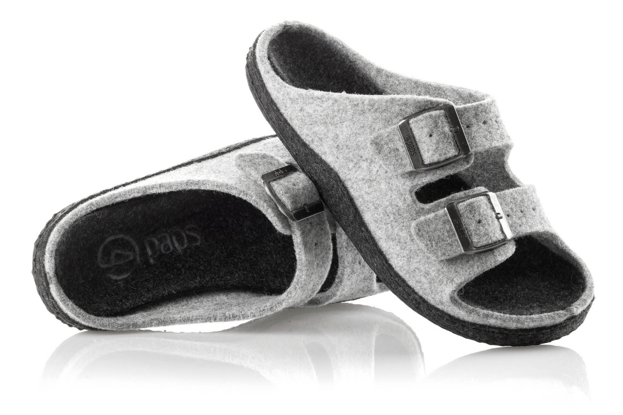 Szare kapcie z dwoma czarnymi sprzączkami, wykonane z filcu, na czarnym podbiciu, ułożone na białym tle.