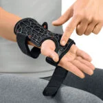 Osoba zakłada czarną opaskę na nadgarstek z wyświetlaczem i paskiem, trzymając rękę na stole.