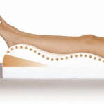 Osoba leży na specjalnym poduszce ortopedycznej wspierającej nogi i kręgosłup, w celu poprawy komfortu i zdrowia.