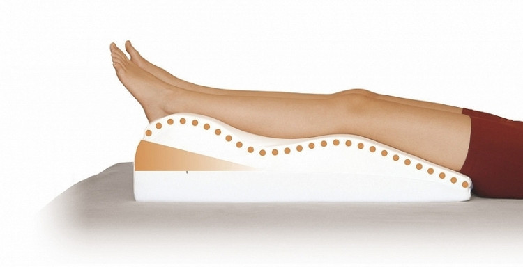 Osoba leży na specjalnym poduszce ortopedycznej wspierającej nogi i kręgosłup, w celu poprawy komfortu i zdrowia.