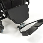 Kółka, czarna poduszka i składane stopki wózka inwalidzkiego na białym tle.