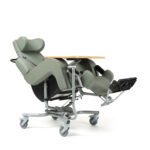 Szpitalny fotel do opieki z podnóżkiem, regulowanym zagłówkiem i drewnianym blatem, na kółkach, w kolorze oliwkowym.