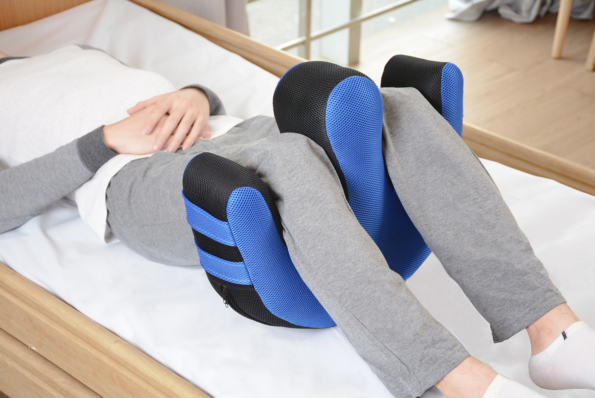 Osoba leżąca na łóżku, korzystająca z poduszki ortopedycznej na kolanach, w domu, w naturalnym świetle.