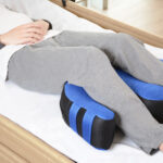 Osoba leżąca na łóżku z poduszkami pod nogami, które wspomagają krążenie i komfort.