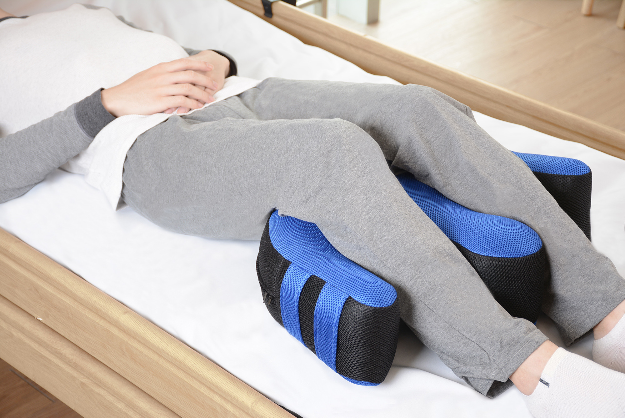 Osoba leżąca na łóżku z poduszkami pod nogami, które wspomagają krążenie i komfort.
