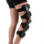 Osoba z unieruchomioną nogą w gipsie i stabilizatorze ortopedycznym na udzie i podudziu.