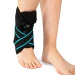 Na nodze opaska elastyczna z czarnym materiałem i niebieskimi paskami, zabezpieczająca kostkę.