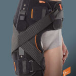 Pas biodrowy ortopedyczny z czarnymi pasami, elementami mocującymi i kieszeniami, na modelu w szarych spodniach.