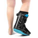 Orteza stawu skokowego na lewej nodze, czarna z niebieskimi elementami, zakładana na stopę i łydkę.