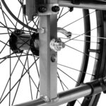 Szczegóły mechanizmu napędu i osi koła wózka inwalidzkiego, z widocznymi metalowymi elementami i szprychami.