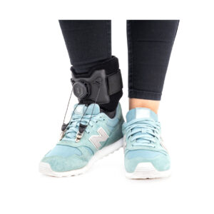 Osoba w czarnych spodniach i jasnoniebieskich butach, nosząca urządzenie wspomagające chodzenie z czujnikiem na kostce.