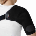 Osoba nosząca czarny stabilizator na ramieniu, z regulowanym paskiem na piersi, w białej koszulce.