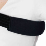 Osoba nosi czarny stabilizator łokcia na białej koszuli.