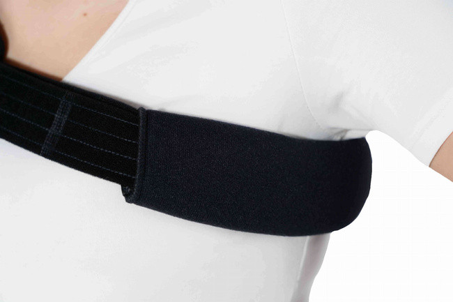 Osoba nosi czarny stabilizator łokcia na białej koszuli.