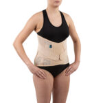 Kobieta nosi czarny top i czarne majtki, na brzuchu ma opaskę ortopedyczną w kolorze beżowym.