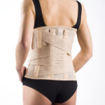 Osoba z czarnym topem i czarnymi majtkami nosi na plecach ortezę lędźwiowo-krzyżową.