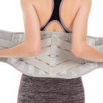 Osoba trzyma szeroki pas ortopedyczny na plecy, ubrana w sportowy top i leggins, przygotowując się do ćwiczeń lub rehabil