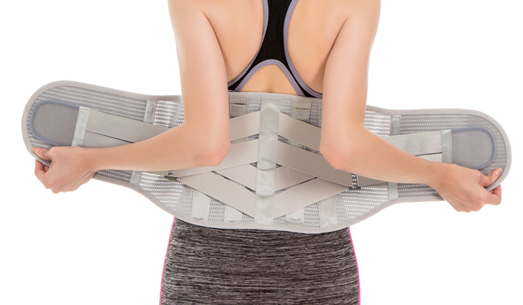 Osoba trzyma szeroki pas ortopedyczny na plecy, ubrana w sportowy top i leggins, przygotowując się do ćwiczeń lub rehabil