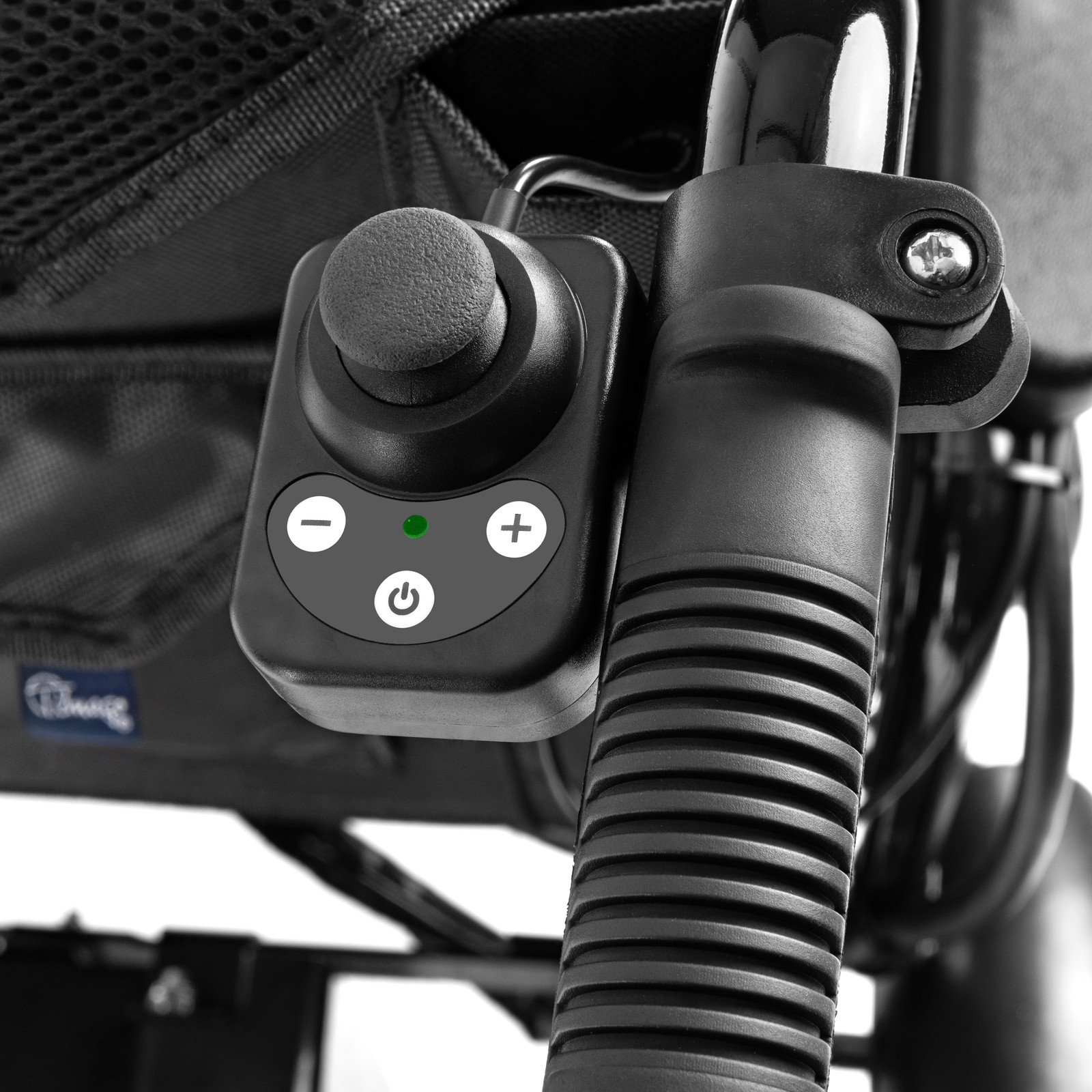 Sterownik elektrycznego wózka inwalidzkiego z przyciskami do regulacji prędkości i włącznikiem, zamontowany na ramieniu.