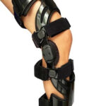 Orteza kolana i nogi z czarnymi paskami i elementami, wspierająca ruch i stabilność kończyny.