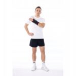 Mężczyzna w sportowym stroju, trzymający rękę na ramieniu, na białym tle, w sportowych butach i skarpetach.