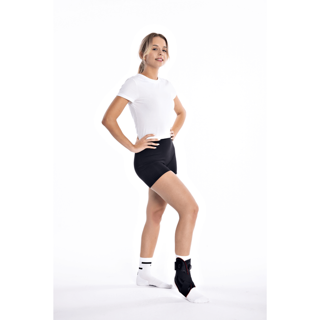 Kobieta w sportowym stroju, stojąca na jednej nodze z uniesioną drugą, uśmiechnięta, na białym tle.