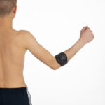 Mężczyzna bez koszulki z opaską na ramieniu zawierającą czujnik, unosi zaciśniętą pięść w geście triumfu lub moty