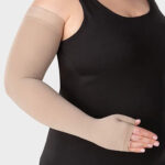 Osoba w czarnym topie i bezuciskowych, beżowych ortezach na rękach, trzymająca się brzucha.