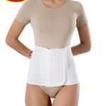 Osoba nosząca białą opaskę lędźwiową, ubrana w beżowy t-shirt i majtki, z rękami za plecami, na tle białego tła.