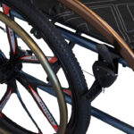 Rama i koła wózka inwalidzkiego z czarnym siedziskiem i metalowymi elementami, widoczne detale konstrukcji.