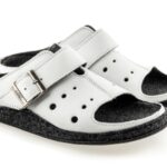 Białe kapcie z czarnymi wstawkami i regulowanym paskiem na rzep, przeznaczone do użytku domowego.